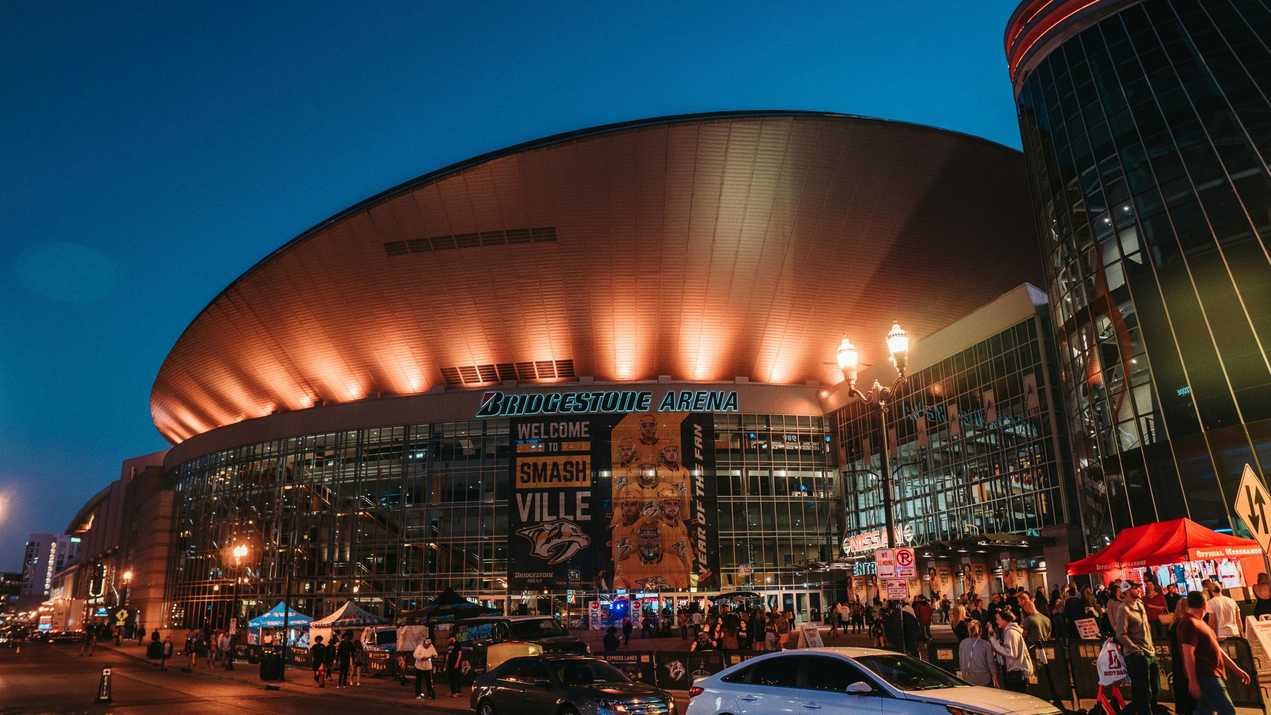 Exterior view of Bridgestone Arena at night in Nashville, Tennessee, with people gathered.