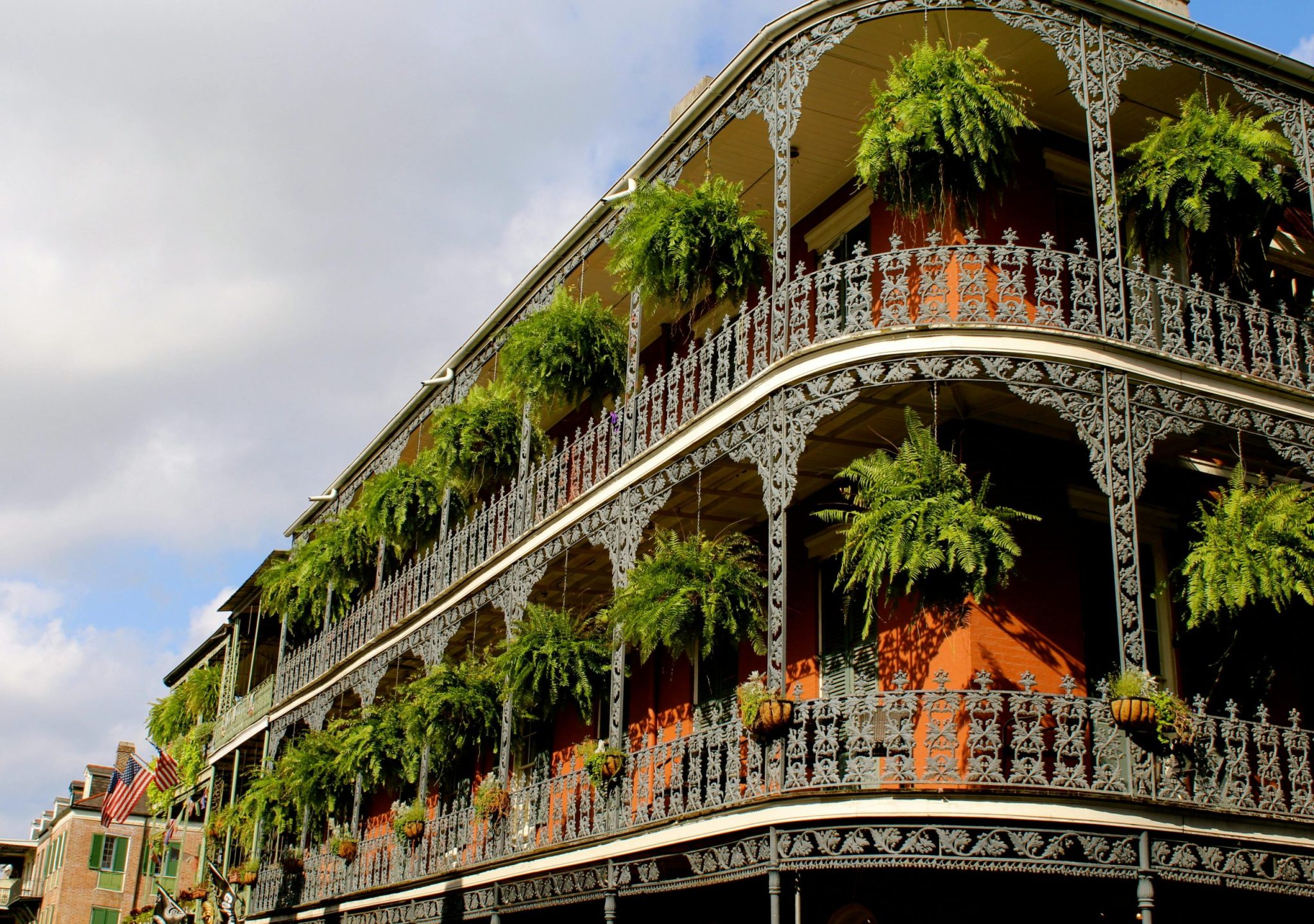 Detailed view of ornate ironwork balconies with lush greenery in New Orleans under a vibrant sky.