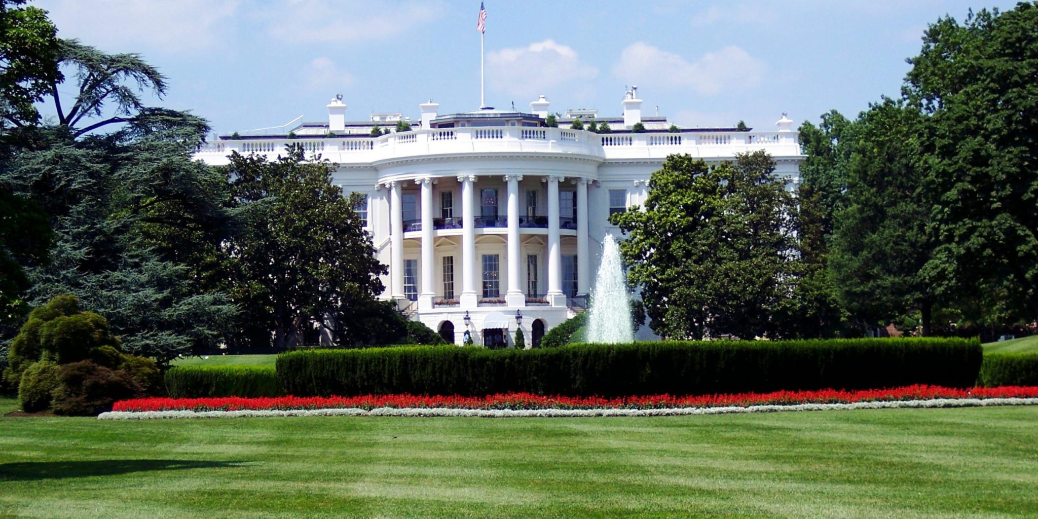 Iconic view of the White House with lush gardens and a central fountain on a sunny day.