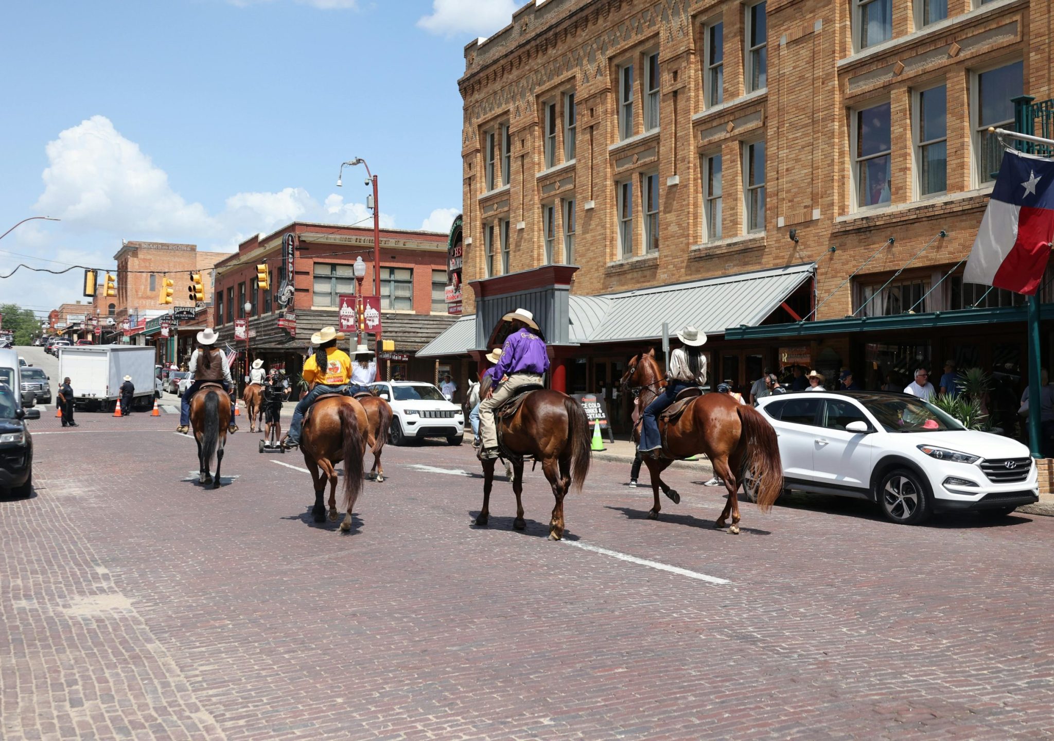 Riders on horseback traverse a historic Fort Worth street lined with vintage architecture.