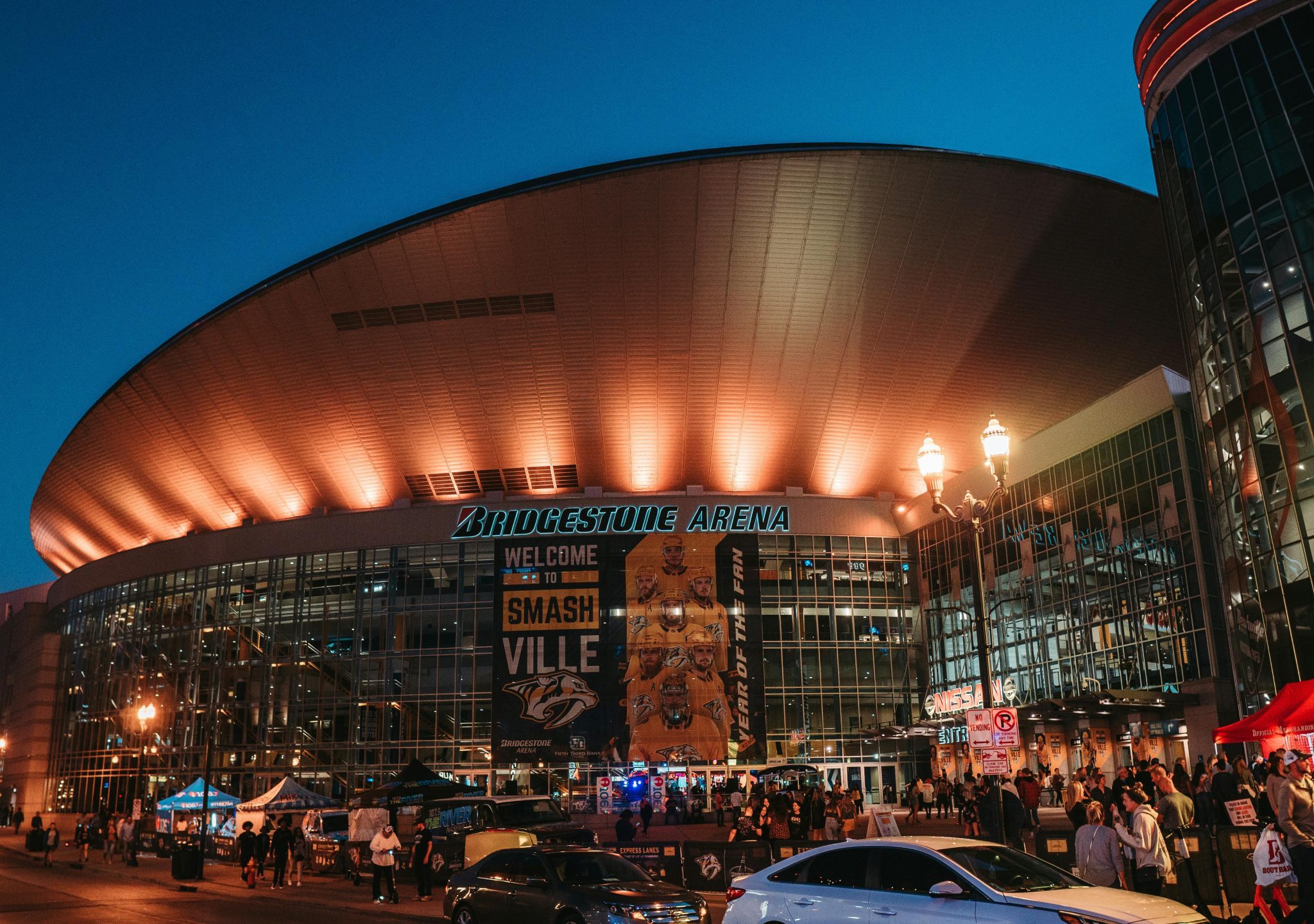 Exterior view of Bridgestone Arena at night in Nashville, Tennessee, with people gathered.
